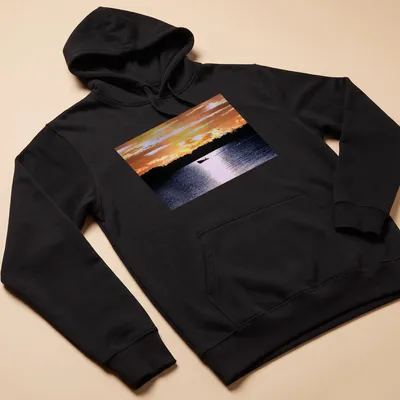 Boat silhouette against a colorful sunset in orange, yellow, and blue — printed on a unisex hoodie