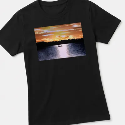 Boat silhouette against a colorful sunset in orange, yellow, and blue — printed on a women's shirt