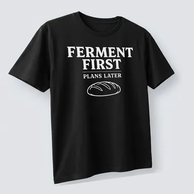 Bold typographic design shirt stating 'FERMENT FIRST PLANS LATER' with sourdough bread imagery — printed on a unisex t-shirt (angled view)