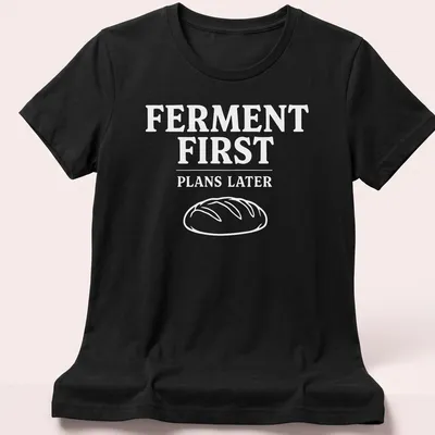 Bold typographic design shirt stating 'FERMENT FIRST PLANS LATER' with sourdough bread imagery — printed on a women's shirt