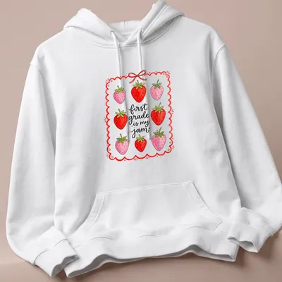 Whimsical illustration of strawberries with text 'first grade is my jam' in red and green — printed on a unisex hoodie