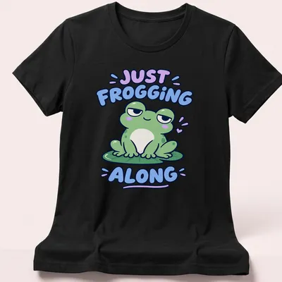 Kawaii design featuring a cute green frog with the phrase Just Frogging Along above it — printed on a women's shirt