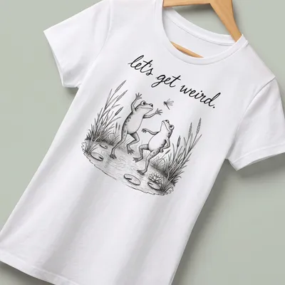 Vintage illustrated frogs dancing under the text 'let's get weird.' in playful font — printed on a women's shirt
