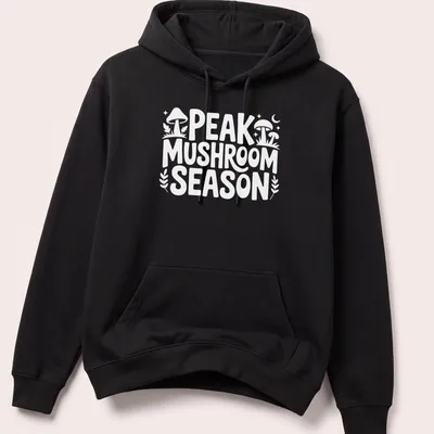 Bold typography Peak Mushroom Season t-shirt featuring mushrooms in green and brown — printed on a unisex hoodie