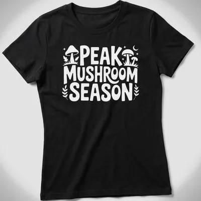 Bold typography Peak Mushroom Season t-shirt featuring mushrooms in green and brown — printed on a women's shirt