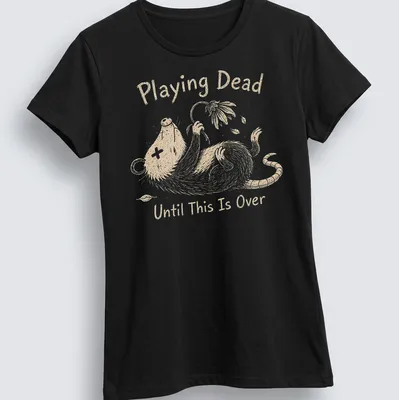 Whimsical illustration of an opossum with the text 'Playing Dead Until This Is Over' in soft colors — printed on a women's shirt