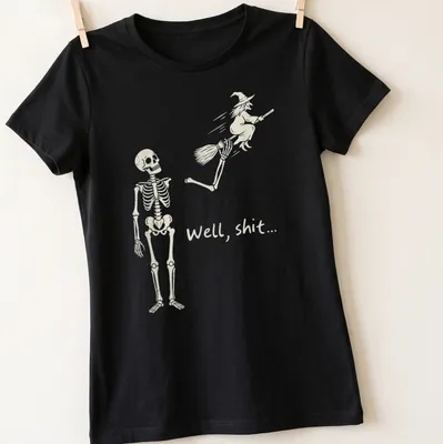 A humorous line-art print of a skeleton reacting to a flying witch with the text 'Well, shit...' — printed on a women's shirt