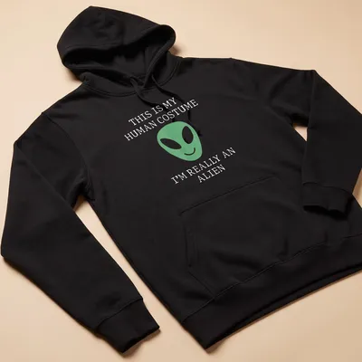 Playful t-shirt featuring a green alien face and humorous text about human costumes. — printed on a unisex hoodie