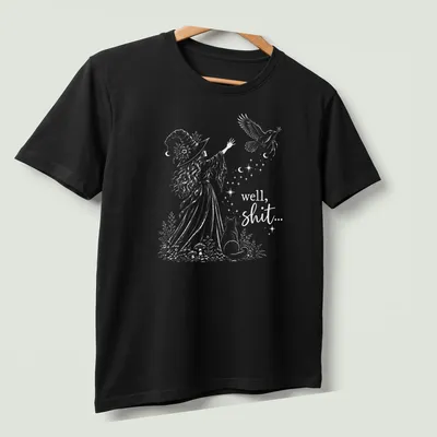 Whimsical illustration of a witch with cat and bird, featuring humorous text — printed on a unisex t-shirt (angled view)